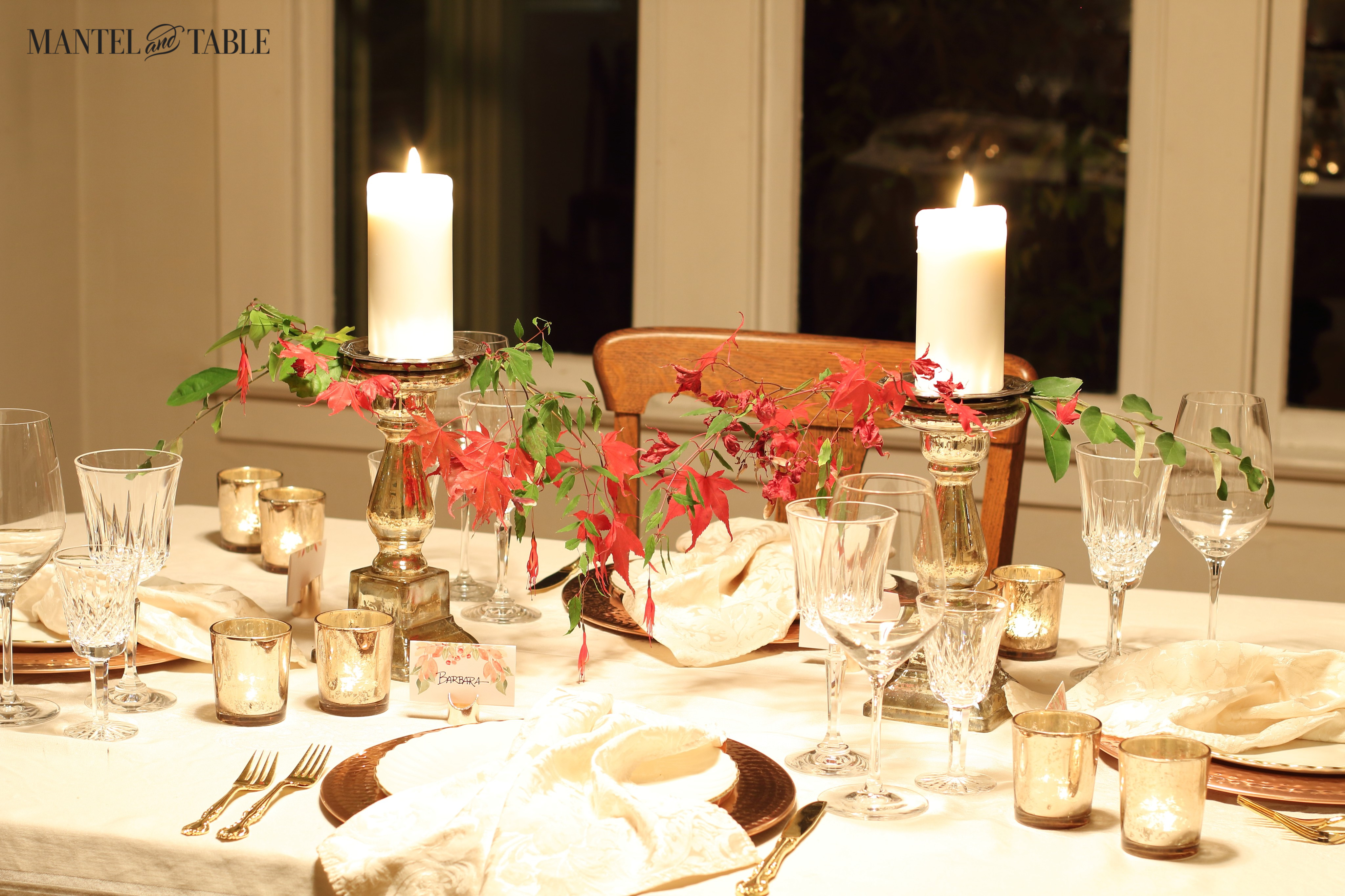 Thanksgiving table with red leaves and fall greenery as a lacy centerpiece draping down from the candlesticks