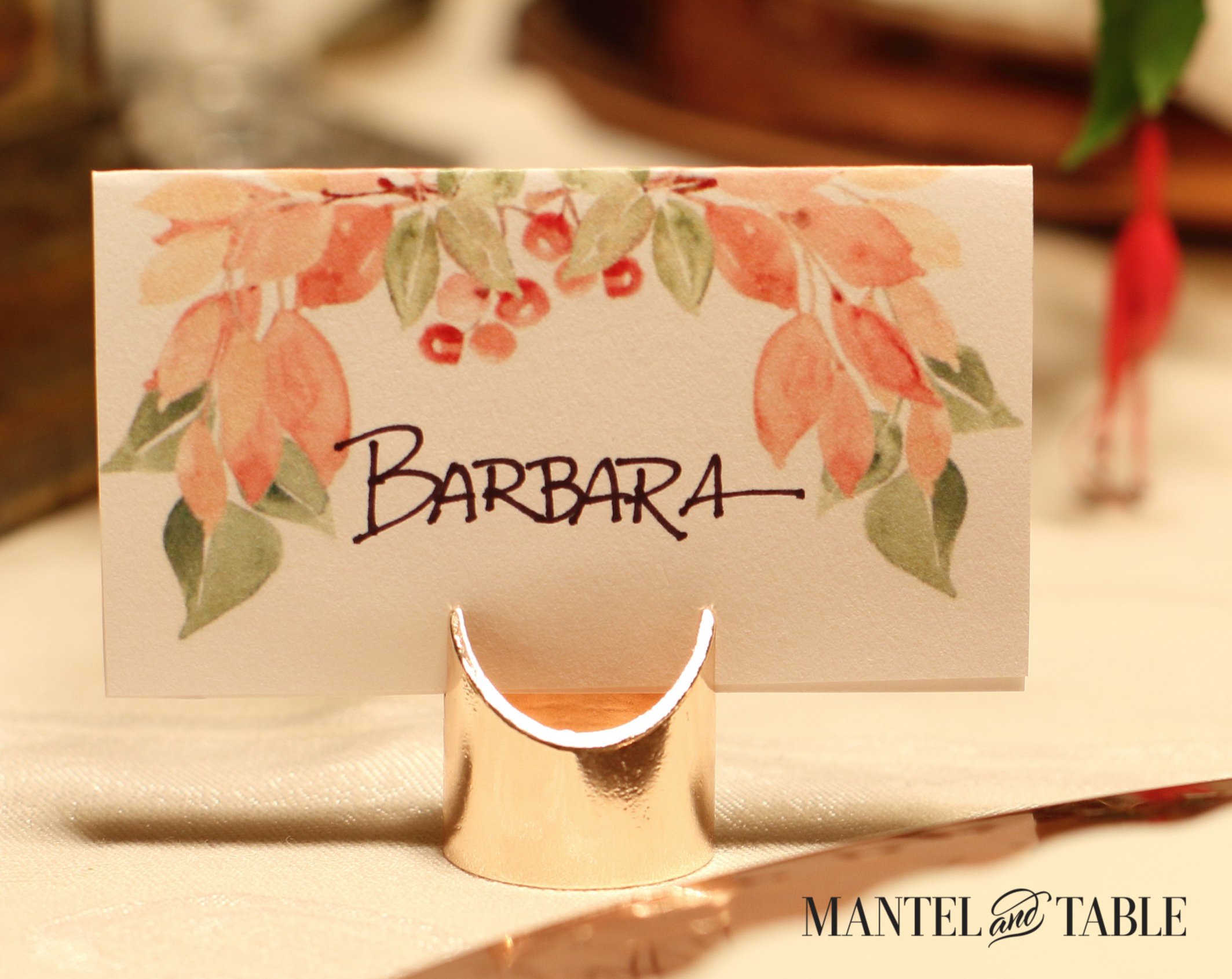 Light orange, green, & red watercolor leaves & berries on white Thanksgiving placecard. Black handwritten name in the middle