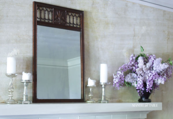 Black amethyst glass vase of lavender lilacs & wisteria on white mantel with brown mirror