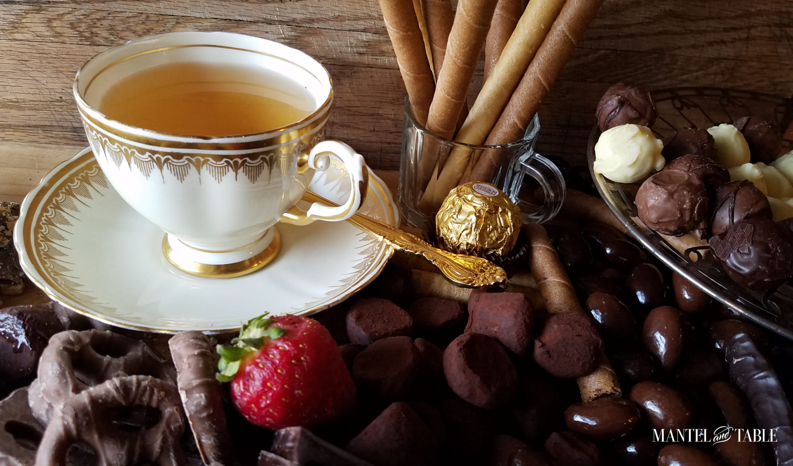 White and gold elegant teacup on breadboard with piles of chocolates and a strawberry