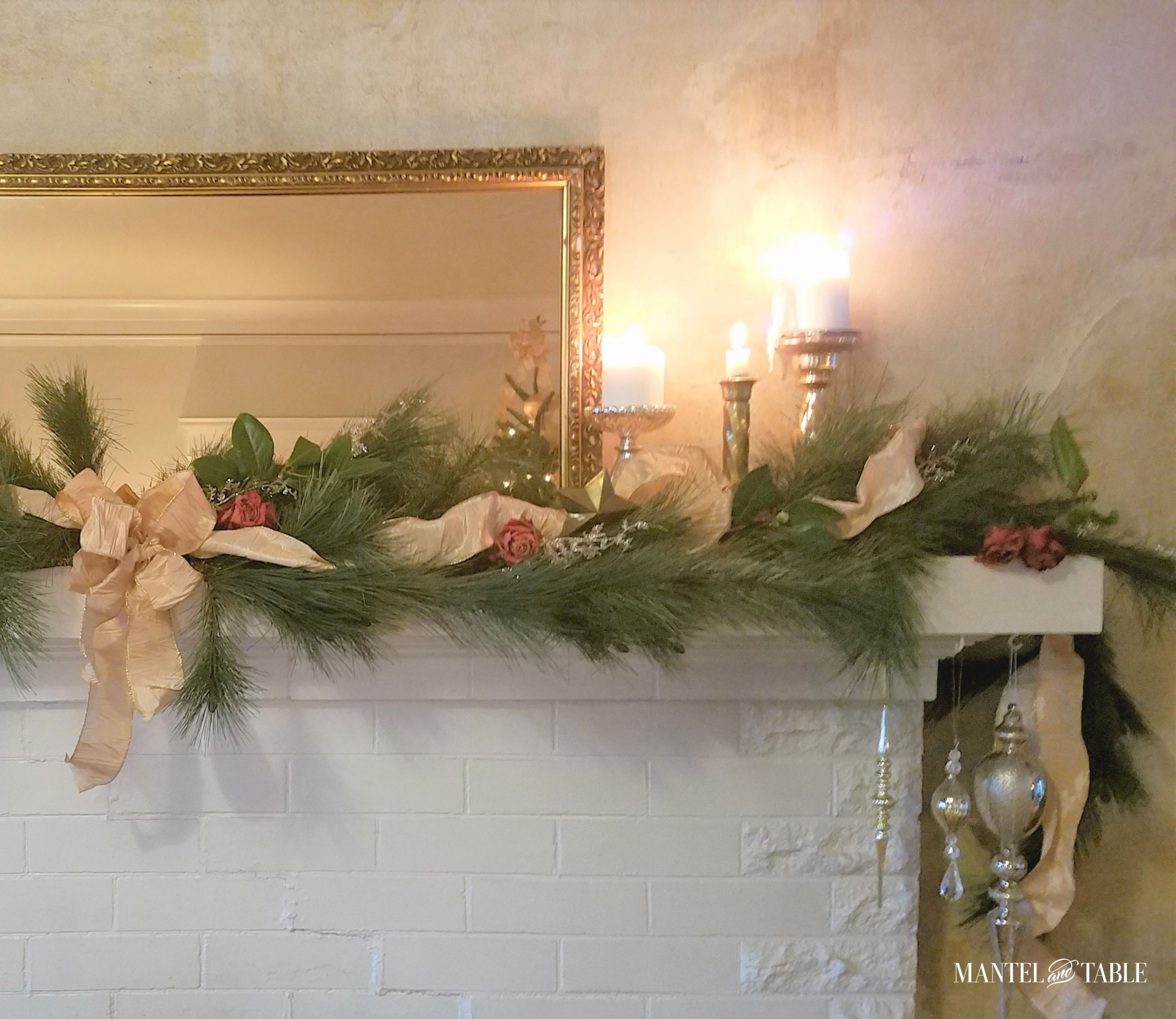 Holiday mantel with gold ribbon, candles, ornaments, and dried roses.