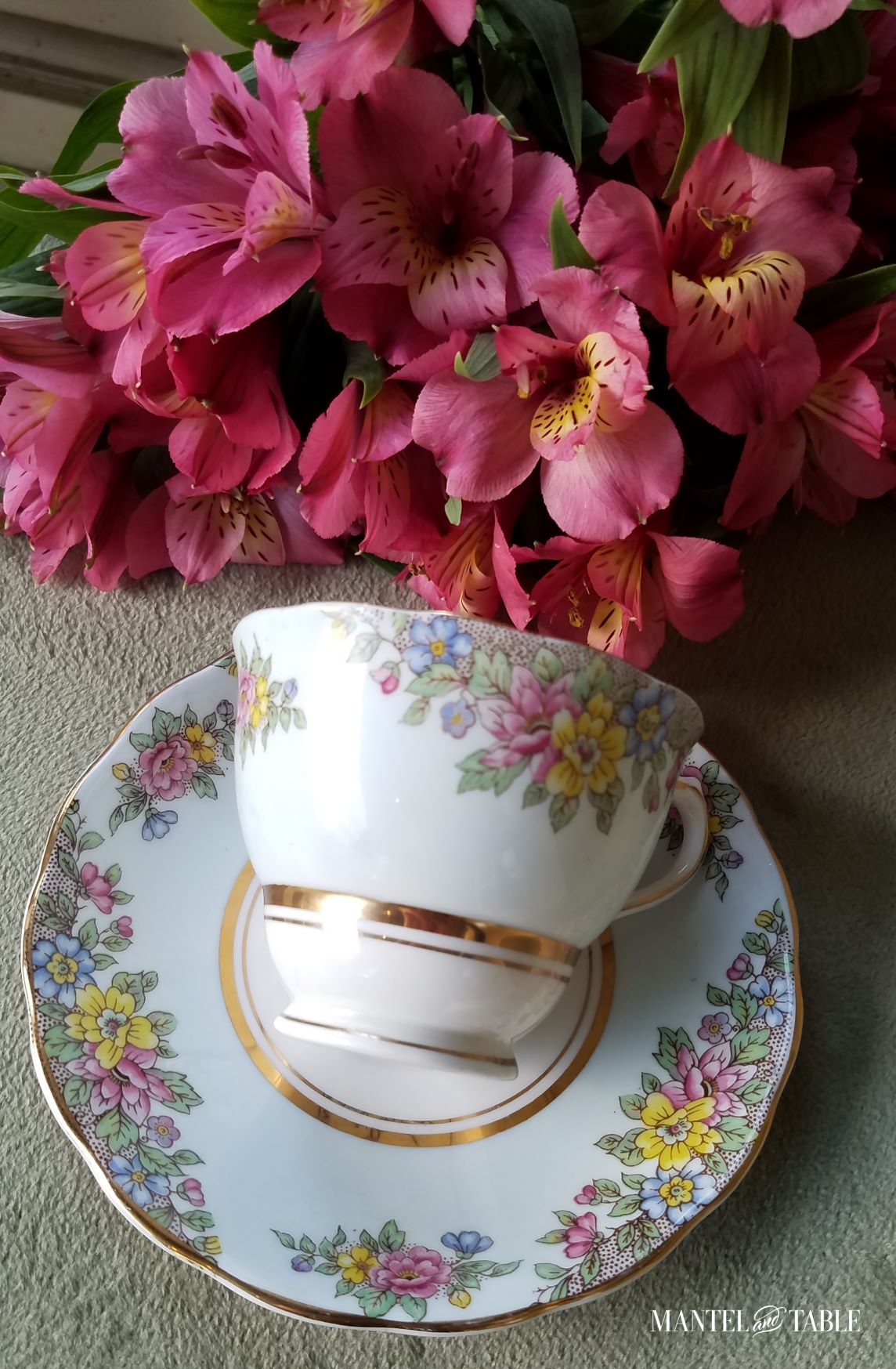 Light blue flowered Colclough teacup lying on saucer. Sage green suede background with pink flowers
