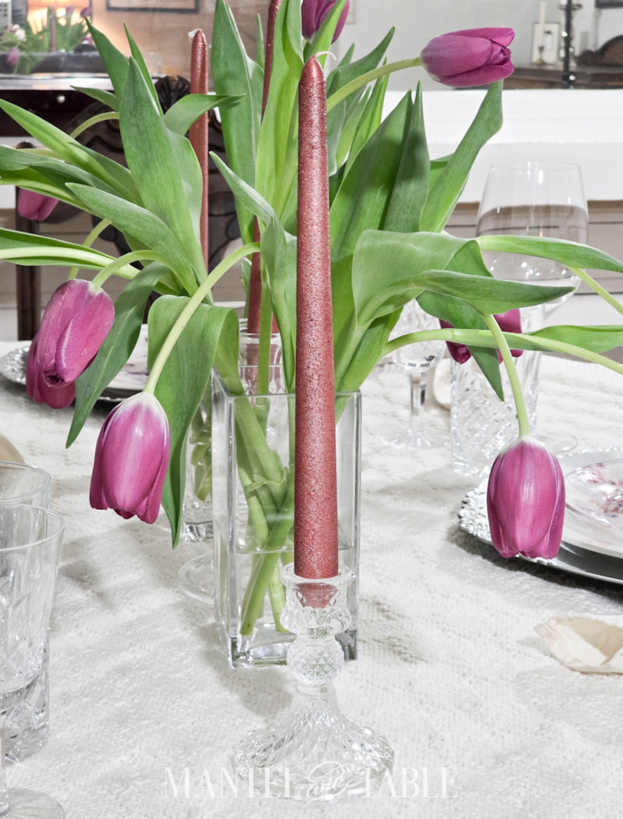 Closeup of a sparkly deep pink taper candle in a crystal holder on a set table